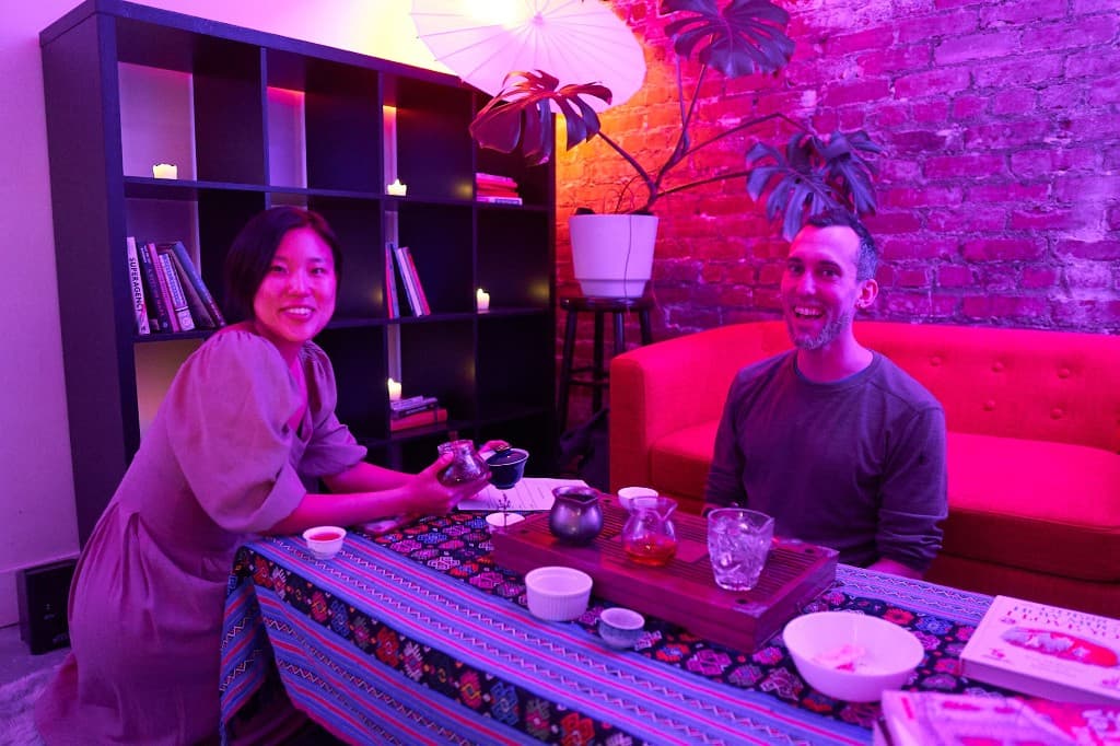 Two people smiling during a tea ceremony with purple and pink lighting